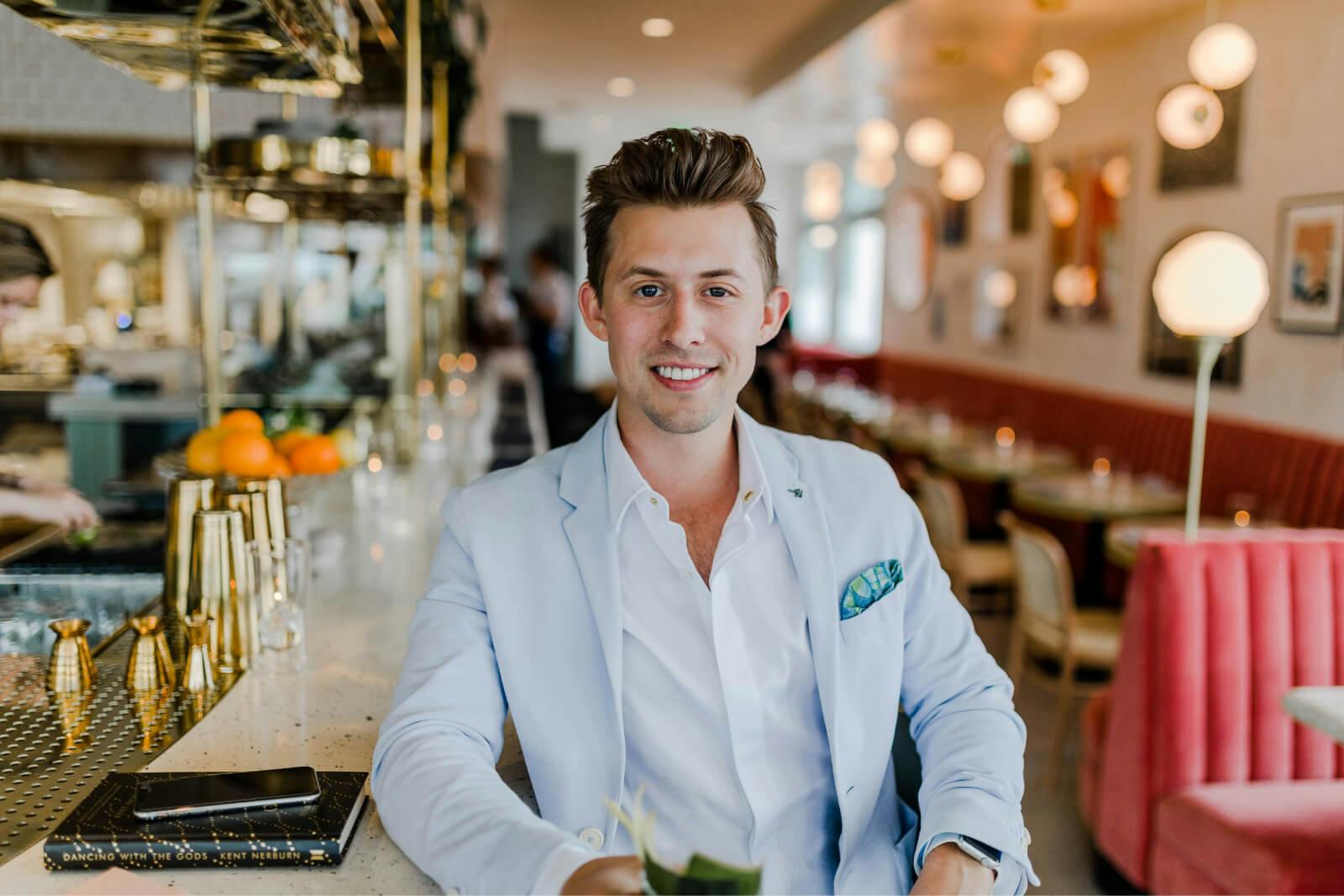 A man in a blue suit jacket smiles at the camera in an empty restaurant